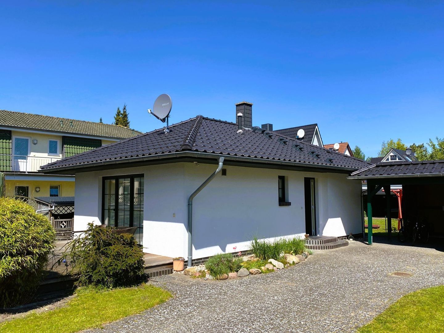 Ein eingeschossiges Haus mit Satellitenschüssel, Schornstein und einer Zuwegung mit Kies.