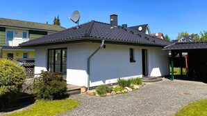 Yhden kerroksen talo, jossa on satelliittiantenni, savupiippu ja sorapäällysteinen ajotie.