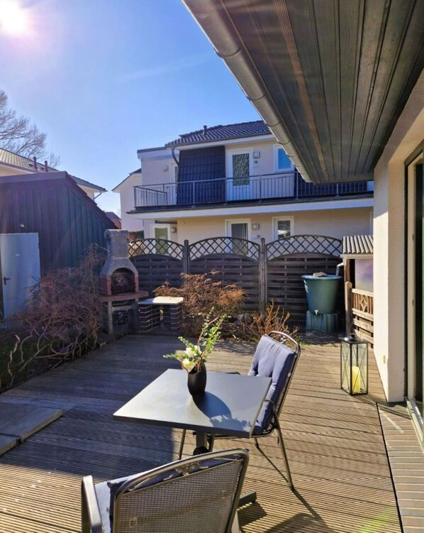 Une terrasse avec une table et des chaises, un pot de fleurs et une vue sur un immeuble doté d’un balcon.