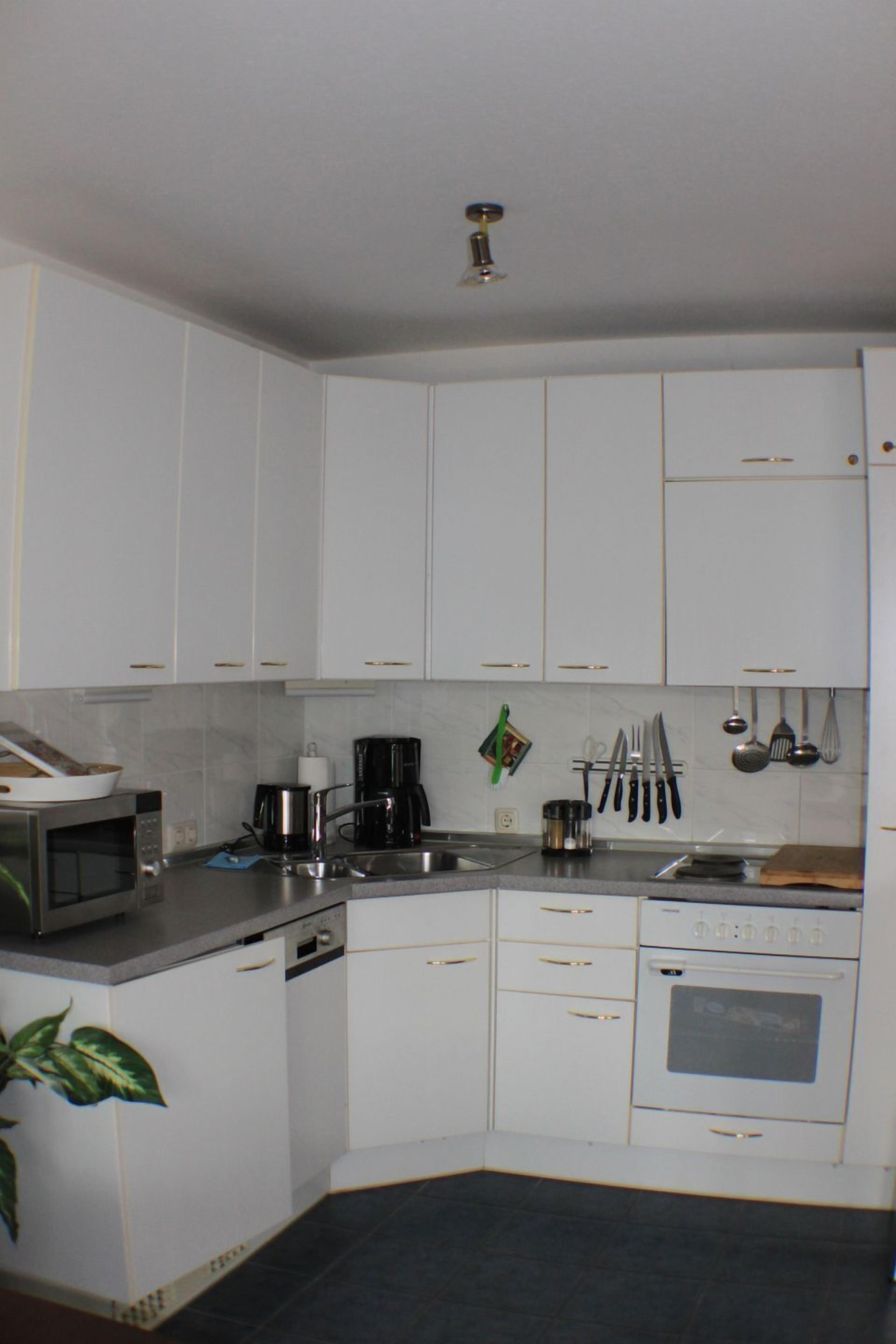 A compact kitchen with white cabinets, a microwave, a coffee maker, and a stove.
