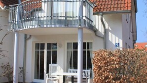 A two-story house with a balcony, a white exterior, and a red-tiled roof.