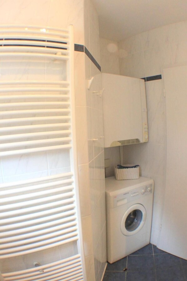 A small laundry room with a washing machine, a drying rack, and a cabinet.