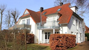 A two-story house with a red-tiled roof, white walls, and a balcony with metal railings.