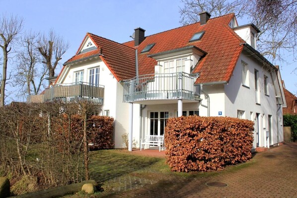 A two-story house with a red-tiled roof, white walls, and a balcony with metal railings.