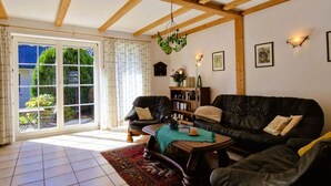 Een ruime woonkamer met een groot raam, een zwarte leren bank, een houten salontafel en een boekenkast.