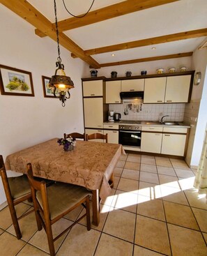 Une cuisine avec des poutres en bois, une table à manger avec des chaises et un luminaire suspendu.
