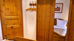Een houten bed met een bruine deken, een houten garderobe en een houten deur met kapstok.