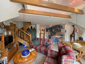 Ein geräumiges Wohnzimmer mit einer karierten Sofagarnitur, einem Holztisch und einer Treppe, die zu einer oberen Ebene führt.