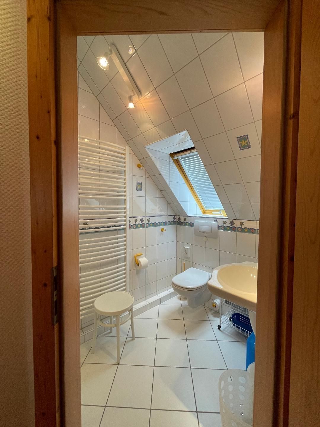 A small, tiled bathroom with a skylight, a toilet, a sink, and a small stool.