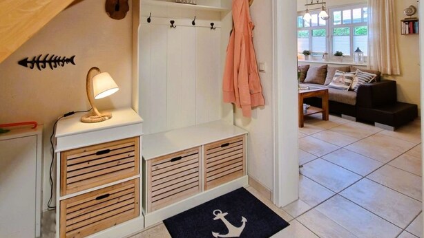 Un escalier avec des rampes en bois menant à un palier où se trouvent un porte-manteau, un banc avec des tiroirs de rangement et une petite table avec une lampe.