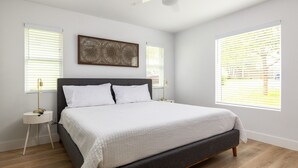 Een moderne slaapkamer met een bed, twee nachtkastjes, een plafondventilator en grote ramen met jaloezieën.