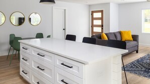 Een moderne woonkamer met een wit eiland, groene stoelen, een grijze bank met gele kussens en zwarte hanglampen.