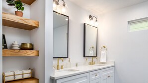 Een moderne badkamer met witte kasten, gouden details en een plant in een potje op een houten plank.