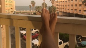 A balcony with a view of palm trees, a parking lot, and buildings in the background. - Just Beachy (Corpus Christi)