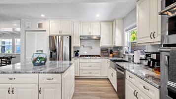 A modern kitchen with white cabinetry, stainless steel appliances, and a marble countertop.