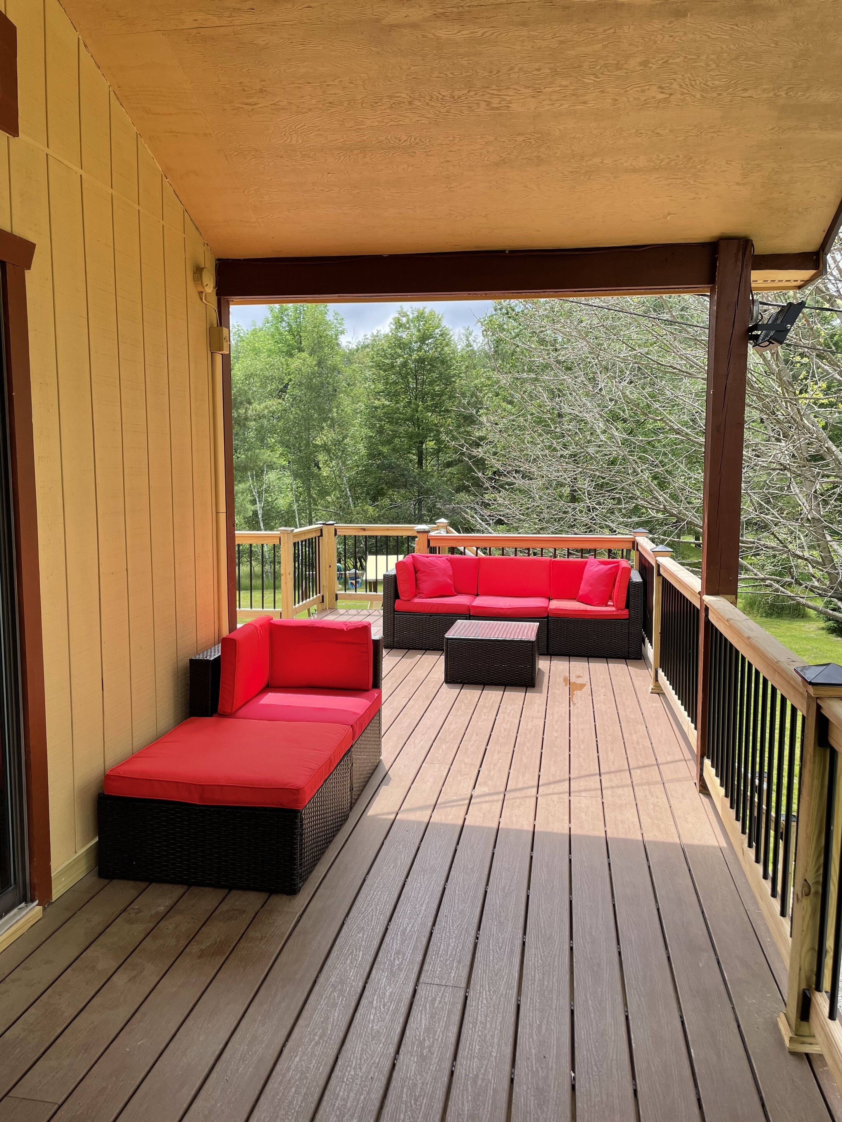 A covered outdoor deck with a red sofa and two black ottomans.