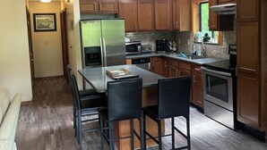 Una cocina moderna con armarios de madera, un refrigerador de acero inoxidable, un horno empotrado y un comedor con mesa y sillas.
