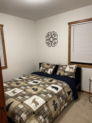 Cozy retreat with a neatly made bed featuring a quilt with animal prints and a geometric wall hanging.