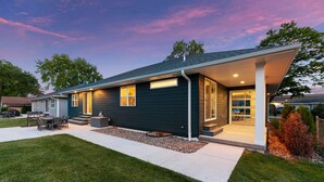 A modern two-story house with a covered porch, a well-maintained lawn, and a patio with outdoor furniture.