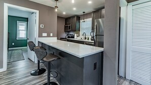 Une cuisine moderne dotée d’un grand îlot central, de tabourets de bar, d’appareils électroménagers en acier inoxydable et de luminaires suspendus.