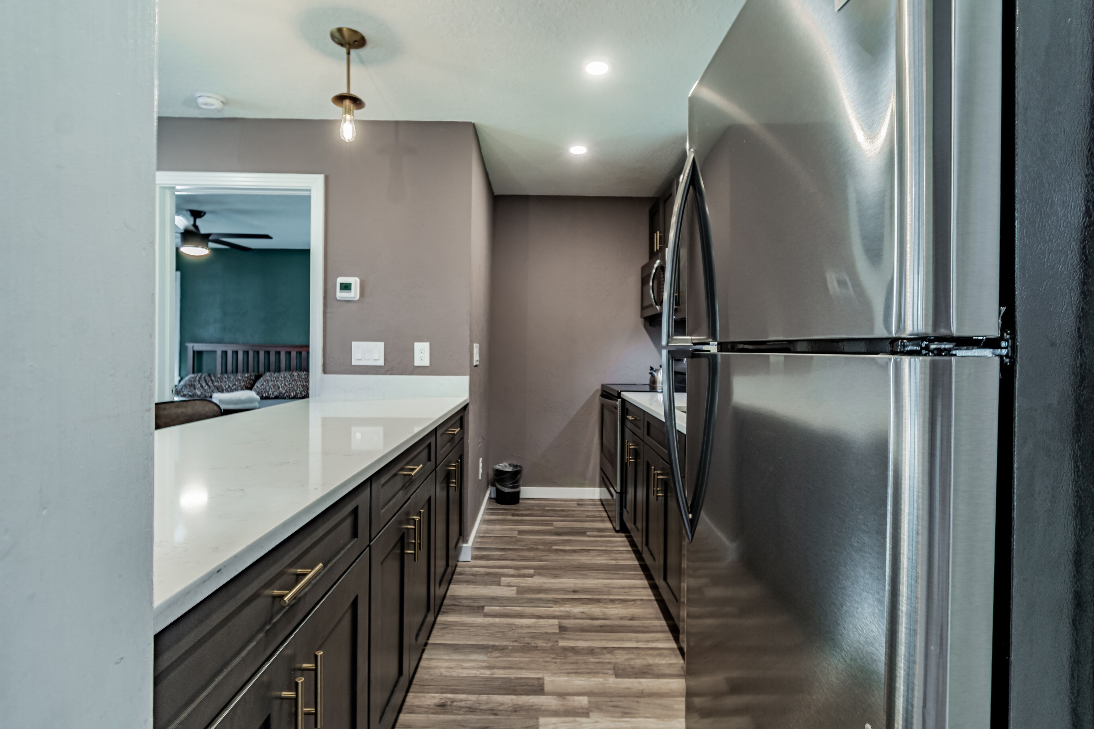 Une cuisine moderne avec des meubles de couleur sombre, un réfrigérateur en acier inoxydable et un plancher en bois.