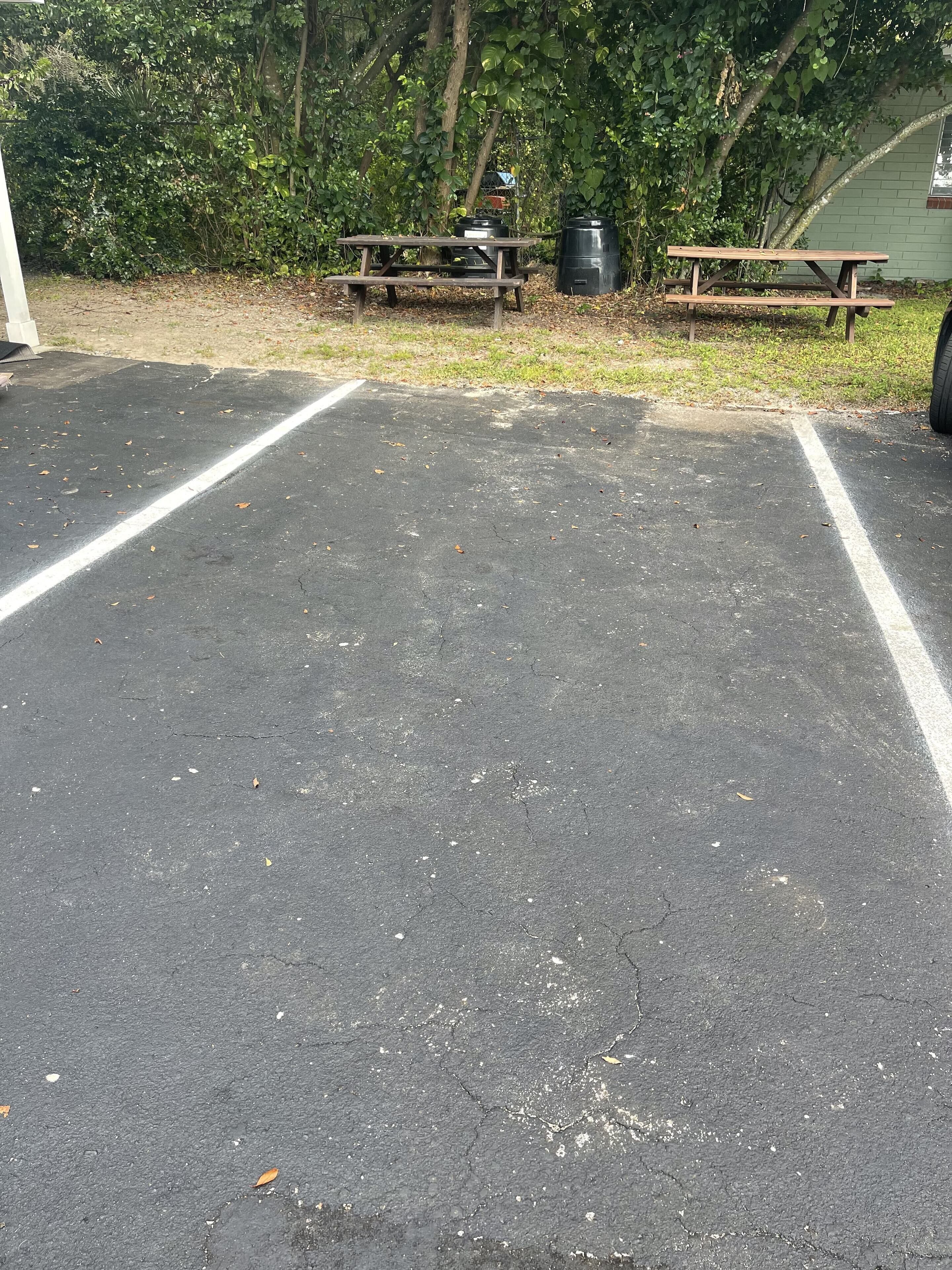 A parking area with two picnic tables and black trash bins.