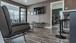 Un salon moderne avec un canapé en cuir, un téléviseur à écran plat et un tabouret de bar.