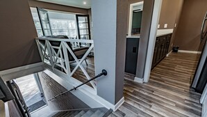 Un intérieur moderne avec un escalier menant à un balcon, un coin cuisine et une vue sur l’extérieur.