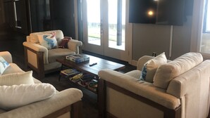 Ein Wohnzimmer mit einer Couch, Sesseln, einem Couchtisch und einem flachbildfernseher an der Wand.