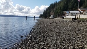 Eine felsige Küstenlinie mit einem Steg, der sich in ruhiges Wasser erstreckt, umgeben von bewaldeten Hügeln.