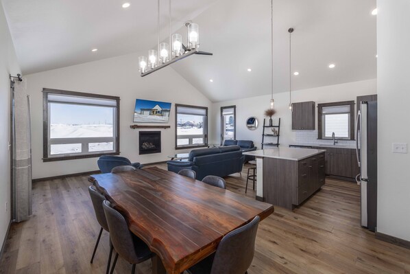 A spacious kitchen with a wooden dining table and chairs, a built-in island, and large windows offering views of a snowy landscape.