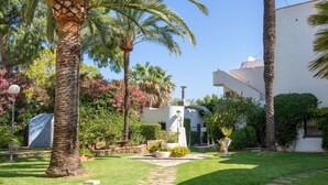 Un jardín bien cuidado con palmeras, un sendero de piedra y un edificio de fachada blanca.