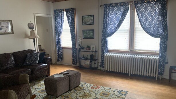Un soggiorno con un divano in pelle marrone, un tappeto decorato, un tavolino e un termosifone.