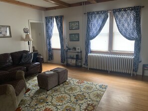 Ein Wohnzimmer mit braunem Ledersofa, einem gemusterten Teppich, einem kleinen Tisch und einer Heizung.