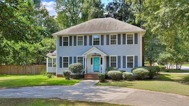A two-story house with a front porch, a blue door, and a well-maintained lawn. - Plantation Styled Home with Sunroom and Large Deck/Yard (Augusta)