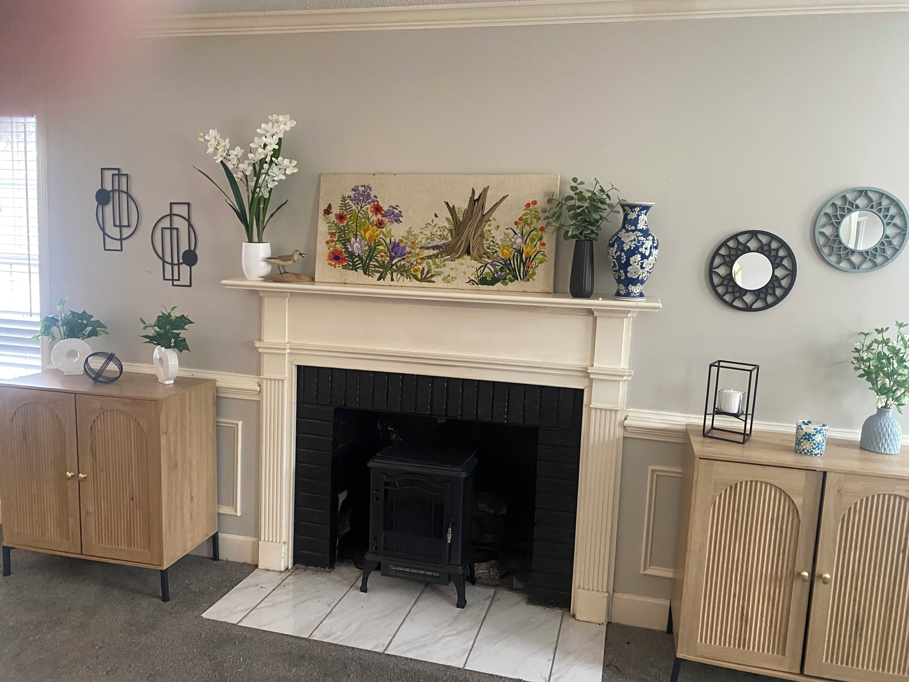 A living room with a fireplace, wooden cabinets, and decorative items including a painting and vases.