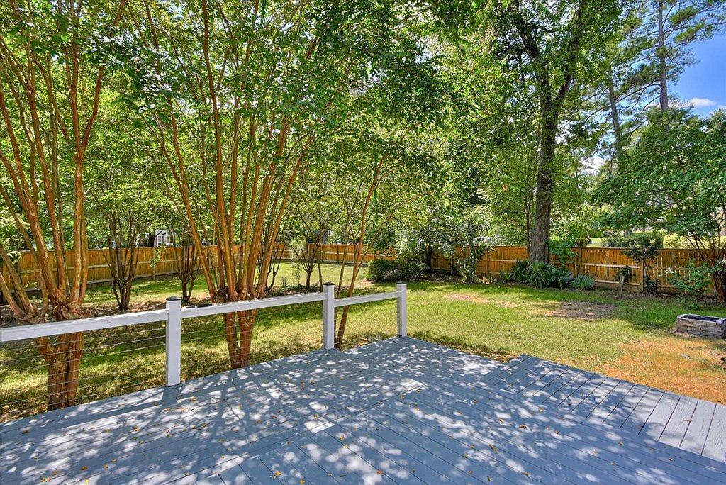 A wooden deck with a white railing, surrounded by lush greenery and a wooden fence.
