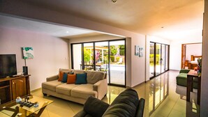 A modern living room with a sofa, a glass coffee table, and a TV on a wooden cabinet. - Comfy and Convenient Home Minutes from Beach National Park (Uvita)