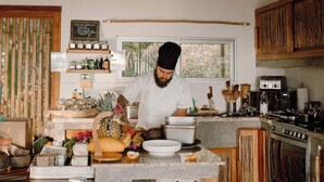 A chef in a kitchen with a stove, pots, and a window. There are jars on a shelf and a sign above the window. - Comfy and Convenient Home Minutes from Beach National Park (Uvita)