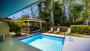 A swimming pool with a tiled deck, surrounded by greenery and a covered seating area. - Comfy and Convenient Home Minutes from Beach National Park (Uvita)