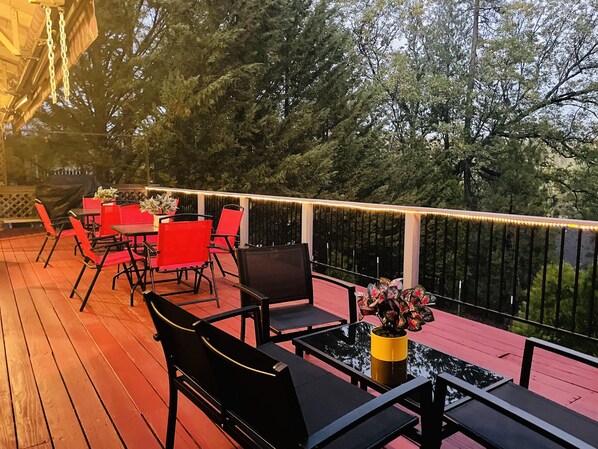 An outdoor deck with red chairs and tables, surrounded by trees and a railing.