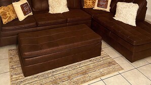 Una sala de estar con un sofá seccional marrón, dos cuadros abstractos grandes y un ventilador de techo.