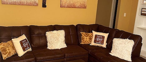 A living room with a brown sectional sofa, two large abstract paintings, and a ceiling fan.