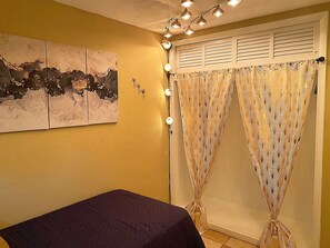 Una habitación con una cama, una lámpara de pared y una cortina estampada.