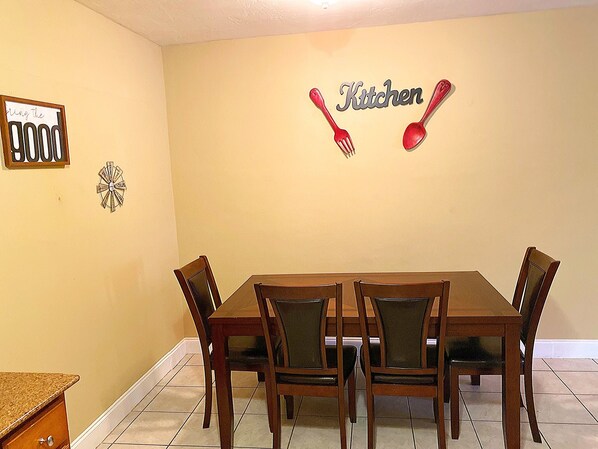 A dining area with a table and chairs, a wall sign reading 'Kitchen,' and a framed picture with text. - Lovely 2 Bedroom Condo With *Free Parking and WiFi*  (Sunrise)