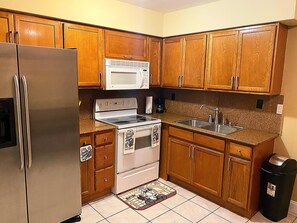 A kitchen with wooden cabinets, a stainless steel refrigerator, a white stove, and a granite countertop.