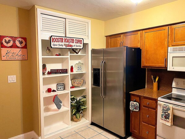 A kitchen with a stainless steel refrigerator, wooden cabinets, and a sign that reads 'ROOSTER ROASTER COFFEE Open Daily at Sunrise.'