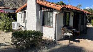 A small house with a tiled roof, a chimney, and a patio with chairs.