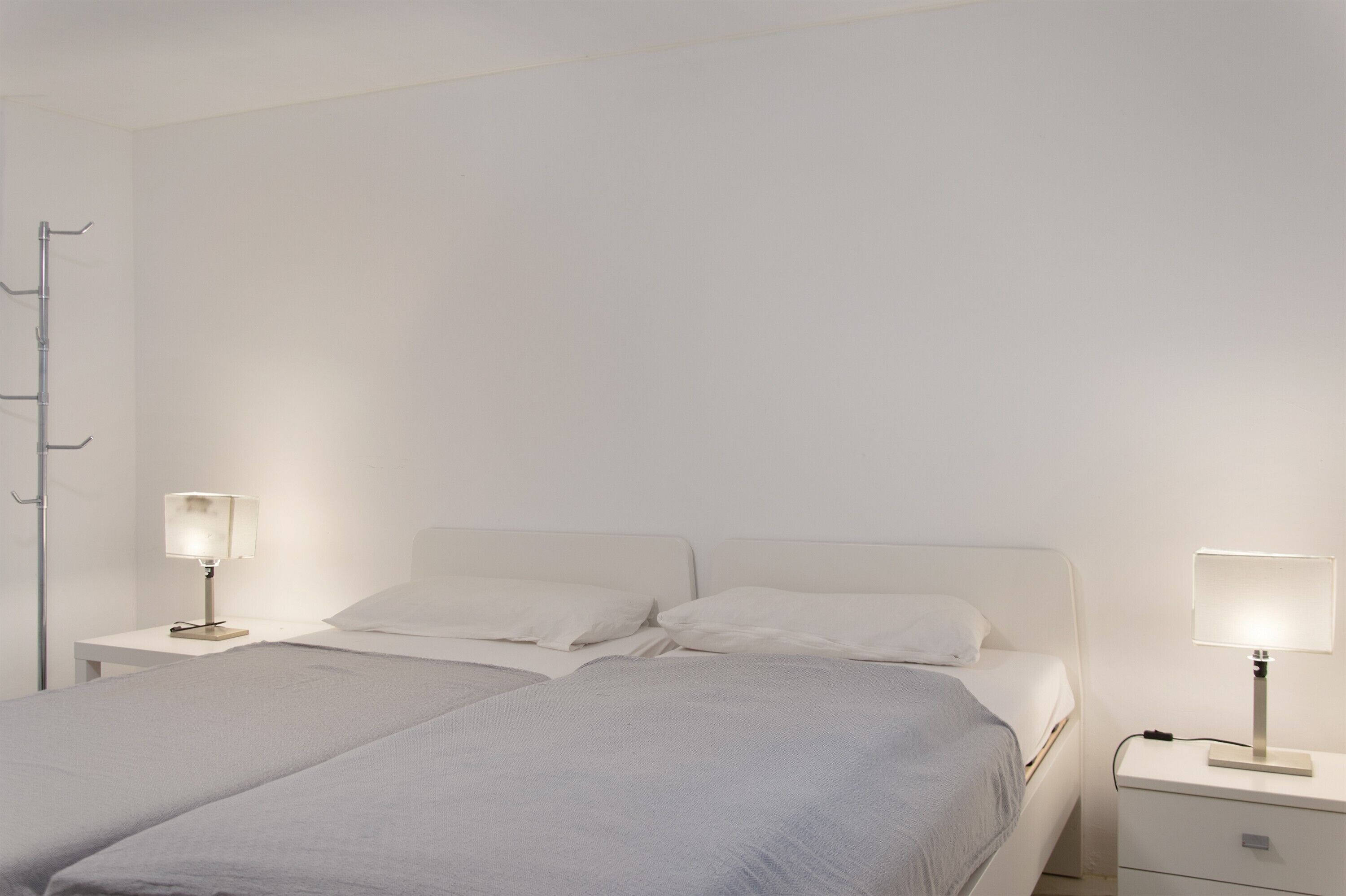Ein Doppelbett mit weißem Kopfteil, zwei Nachttische mit Lampen und eine weiße Wand.