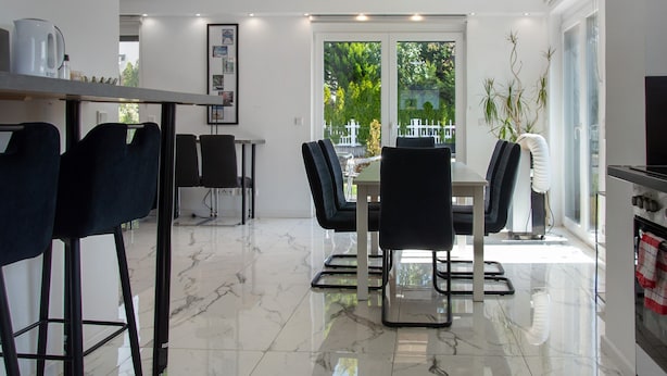 A modern kitchen with a dining area, large windows, and a view of greenery.